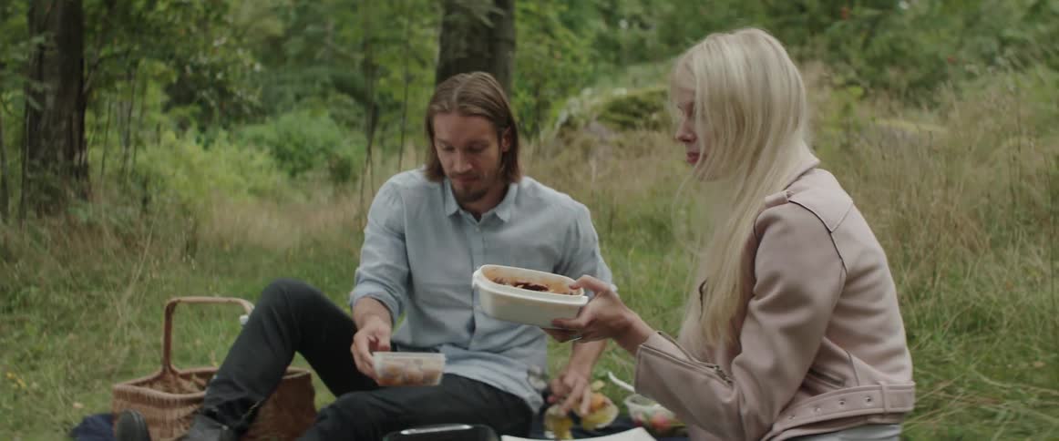A couple are sharing dishes during a picnic outside in daylight