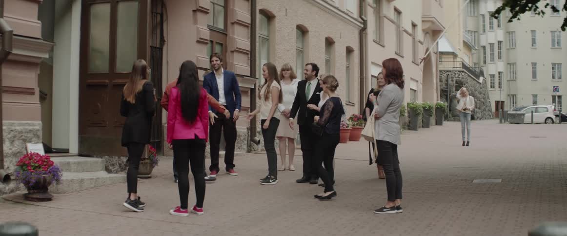 A group of young adults gathers and socializes outdoors on a city sidewalk.