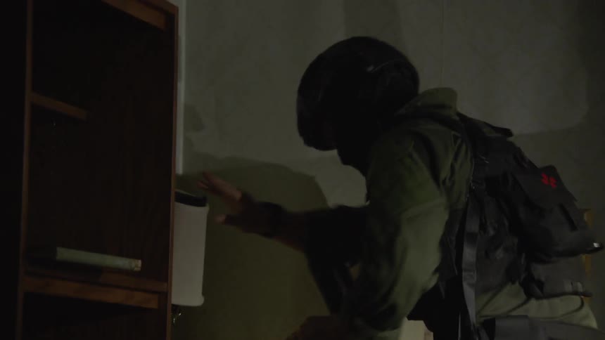 Man wearing a helmet and backpack searches for something in a living room