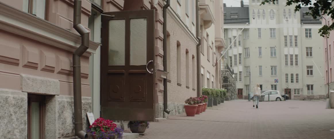 A blonde woman carrying a handbag walks along a cobblestone street near apartments.