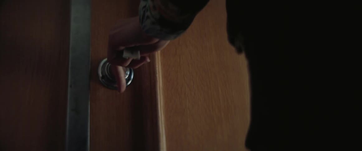 A person uses a key to unlock a wooden door and open it.