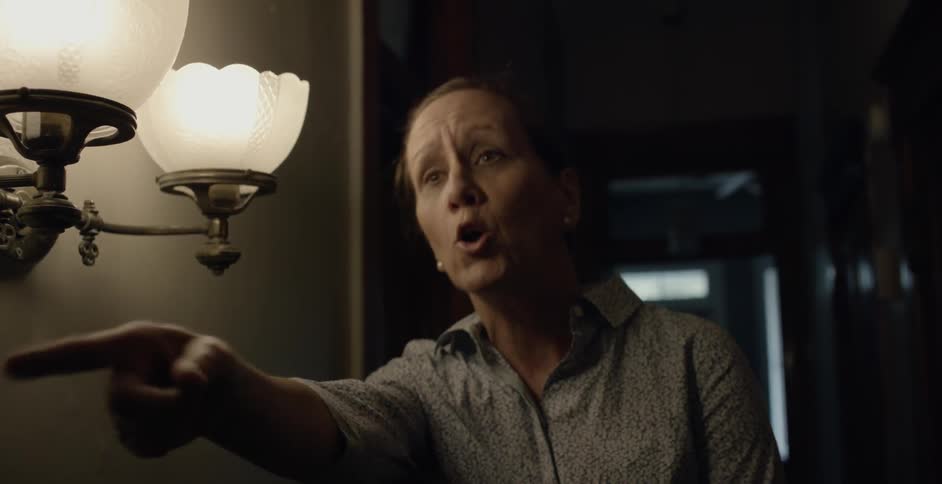 A woman yells points and gestures at someone in a hallway