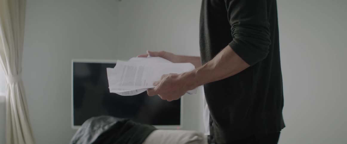 Man in living room puts laptop and pile of papers into backpack