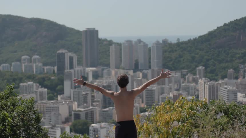 A man raises his arms on the hill above the city
