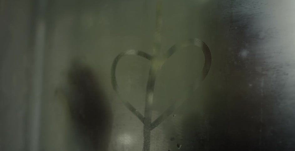 A woman draws a heart on a window and touches the glass