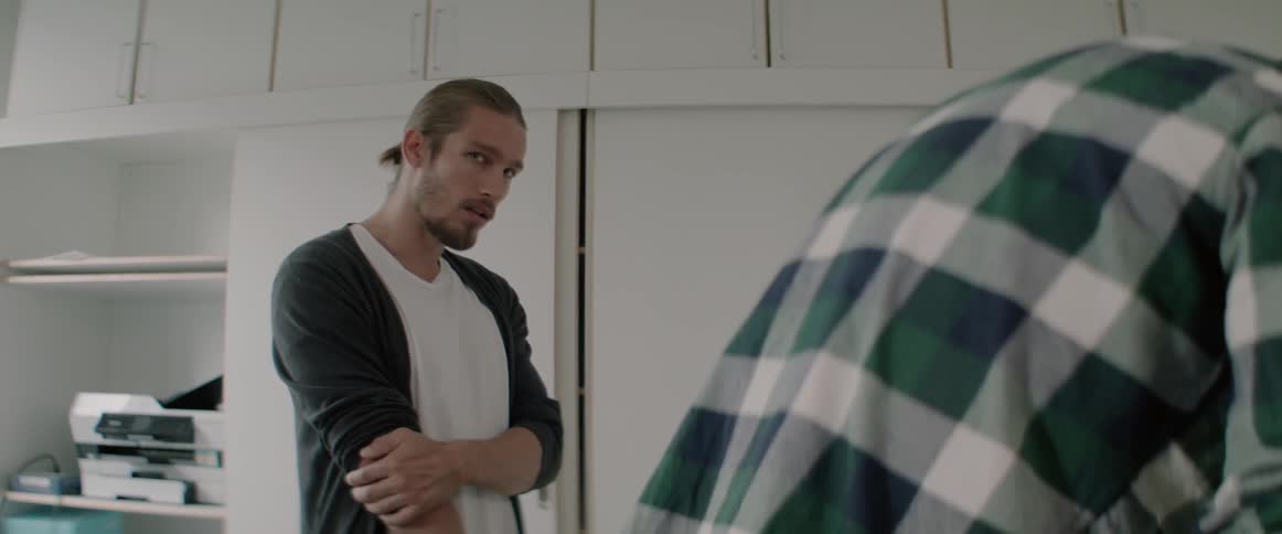 A serious young man stands with crossed arms talking to a male colleague.