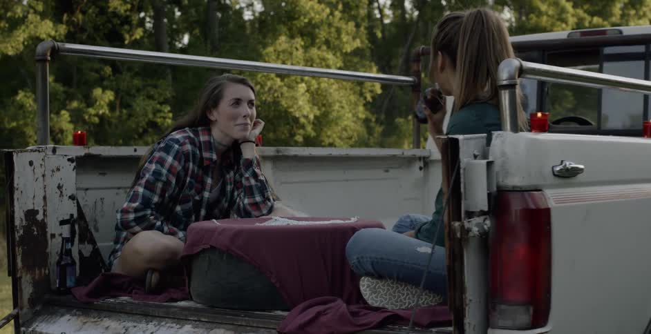 Two women sit in the back of a pickup truck as they drink beer