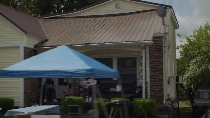 People sit on the front porch with tables and tent set up in the yard