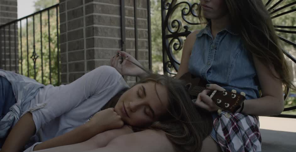 A woman sits by the fence brushing another woman's hair