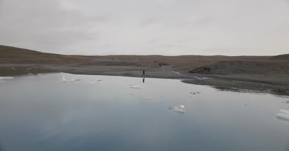 A person walks along the water's edge where chunks of ice float