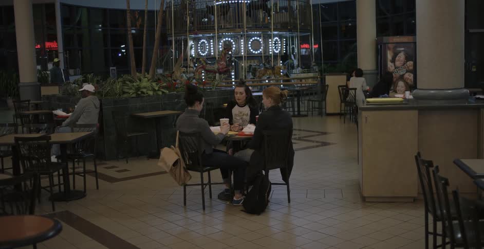 Three women sit at a table in dining court and talk while eating