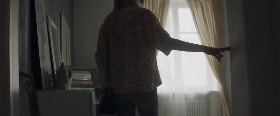 A woman is slowly walking into a living room and looking around in daylight