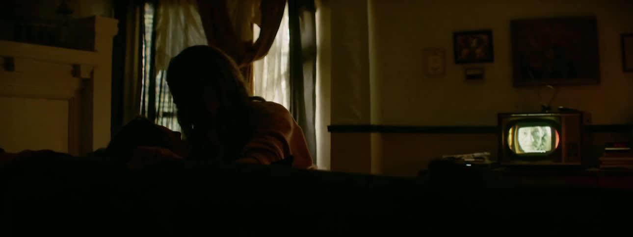 A woman crawls on a man's lap in the dark living room