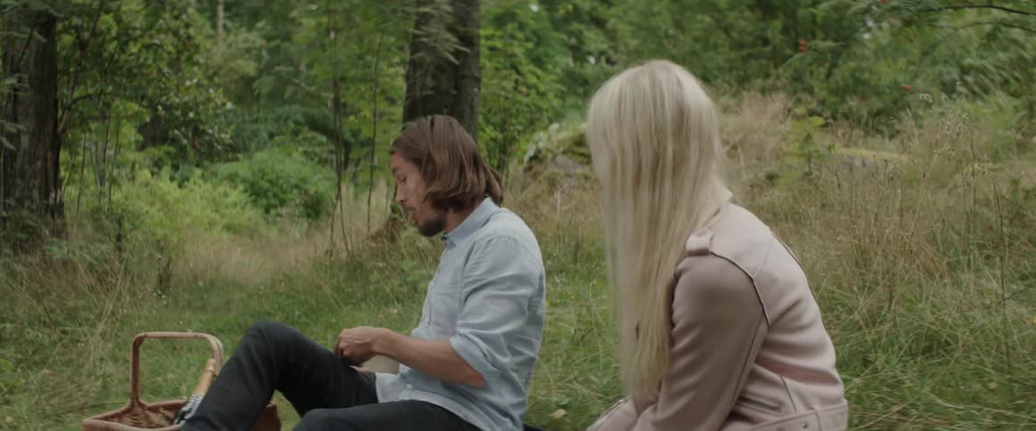 A man and a blonde woman talk while sitting on a picnic blanket.