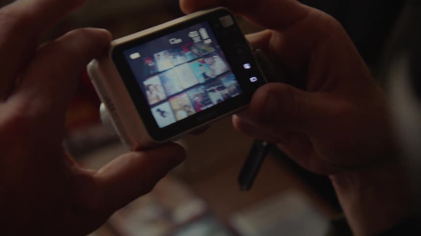A man wearing a mask uses a digital camera to take a picture of items on a table