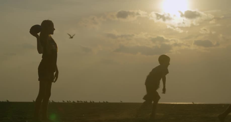 Children play with a football at sunset