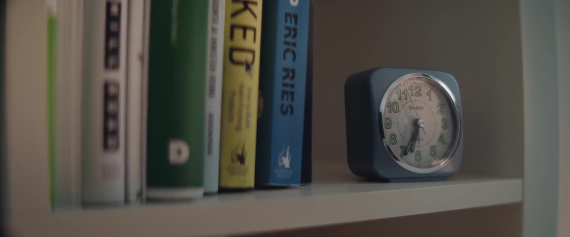 A small alarm clock sitting on a bookshelf next to colorful books.