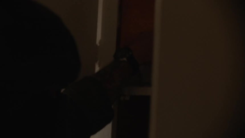 A police officer in tactical gear searches a kitchen cabinet