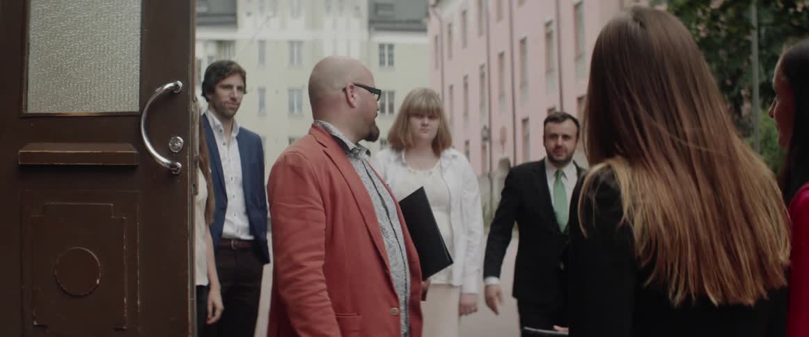 People in professional attire gather and chat near an open wooden apartment door.