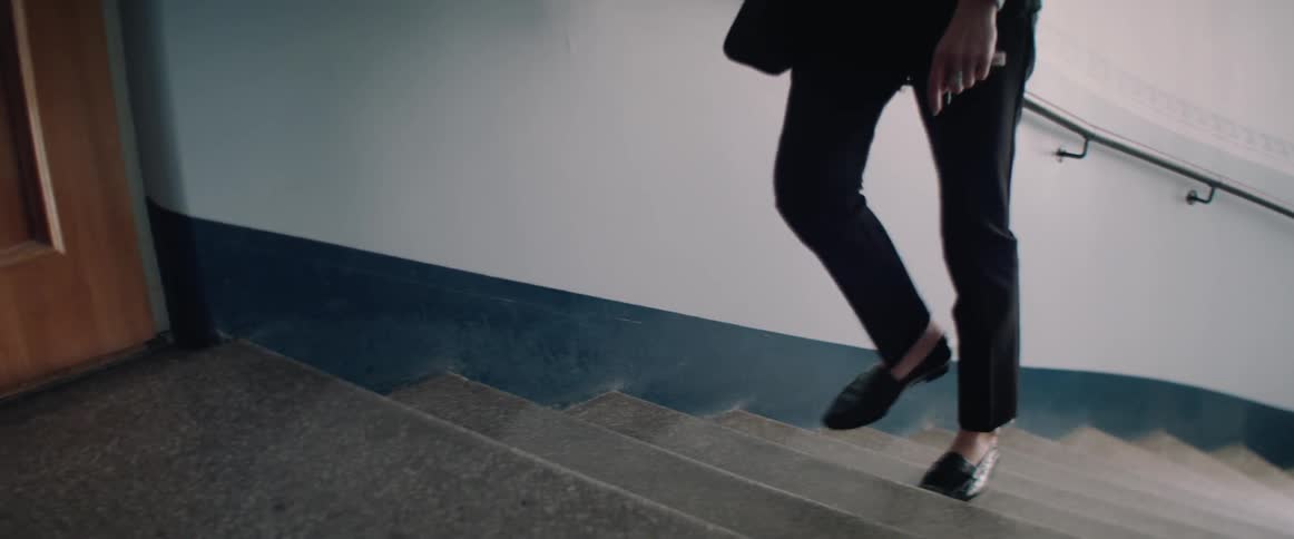 A person wearing black trousers and loafers slowly walks up indoor concrete stairs.