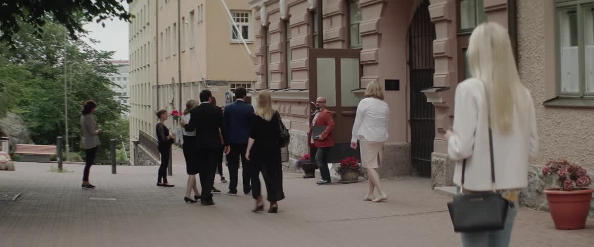 A group of business people walking and gathering outside an apartment building entrance.
