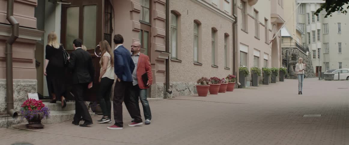 A group of stylishly dressed people walks into a classic city apartment building.