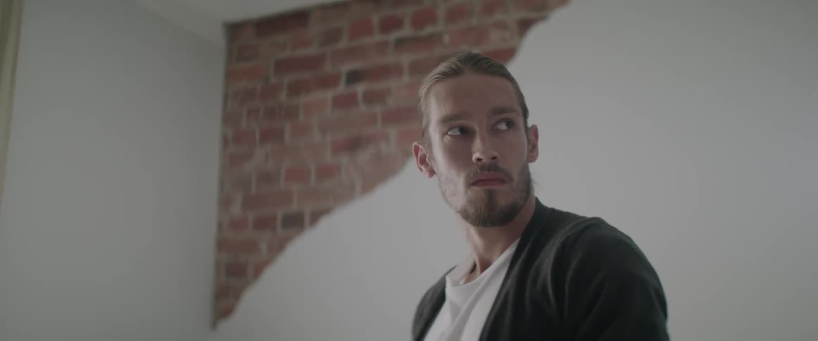 A young man stands up and looks over his shoulder inside a modern room.