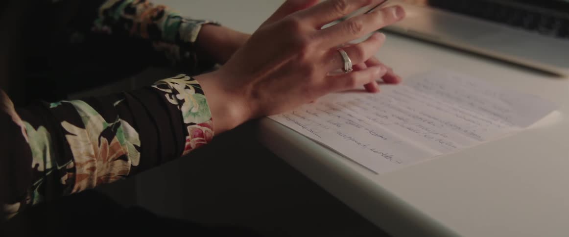A woman holds a pen over a written document while working at desk.