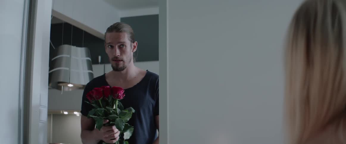 A man pauses in a doorway holding roses then walks into the room