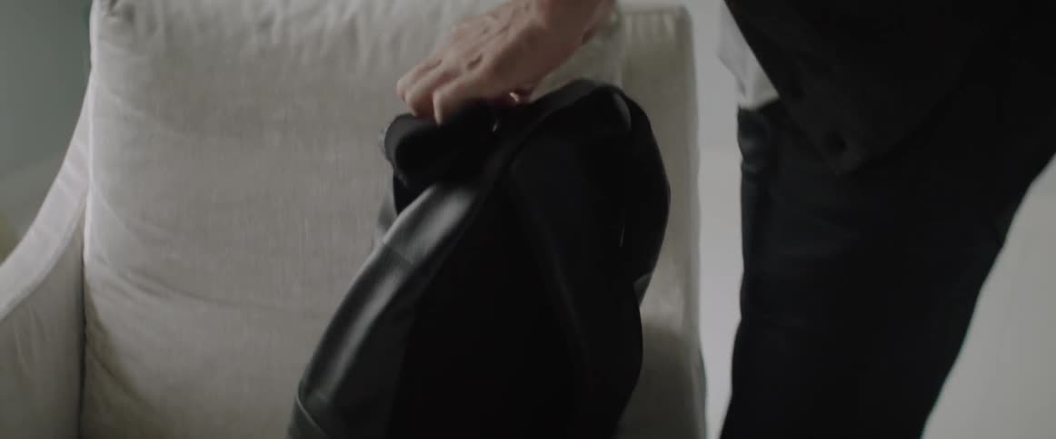 A young man packs his black backpack and prepares to leave the room.
