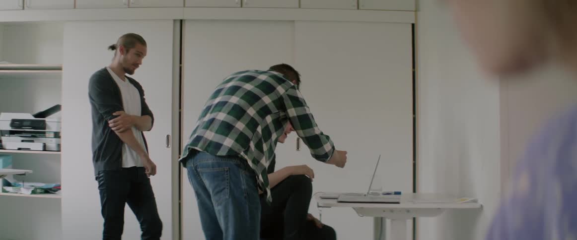 Young men gather around a desk to look at a computer screen together.