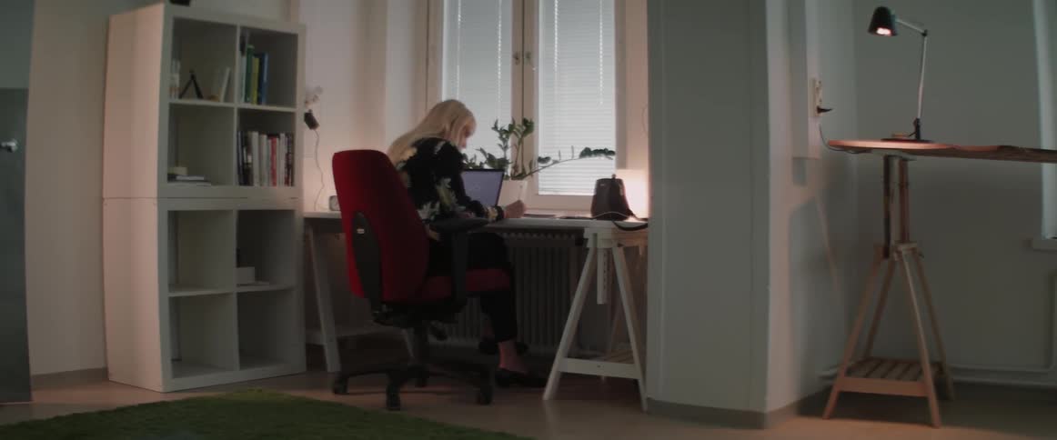 A blonde woman works at a home office desk in front of a window.