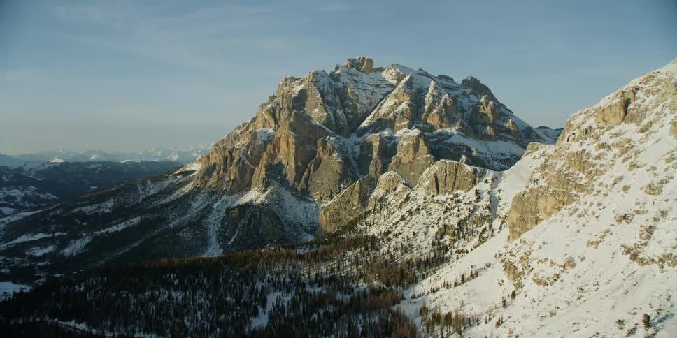 Mountains partially covered in trees and snow on sunny day