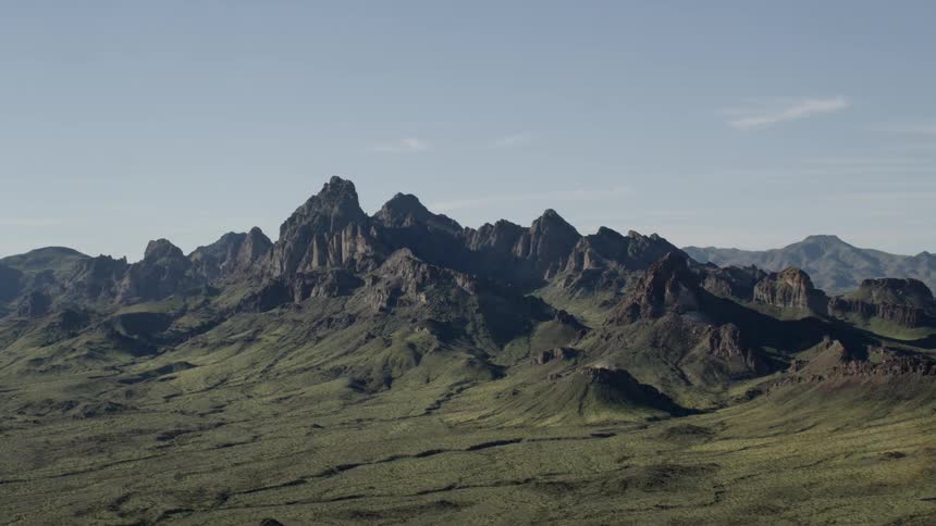 Jagged dark mountains covered in green on clear day