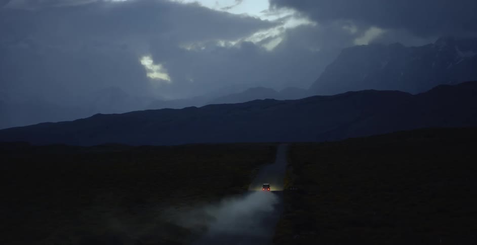 A vehicle drives down a dirt road at night