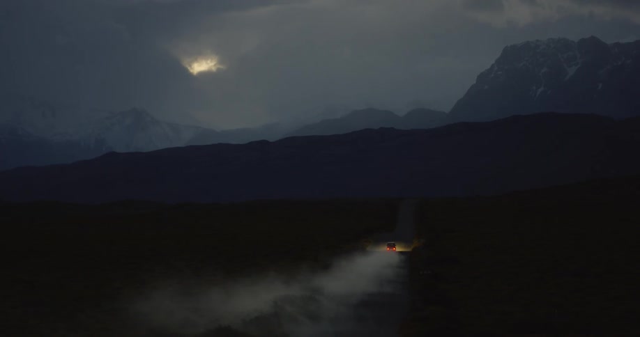 An suv is speeding along a dirt road in a remote landscape at dusk