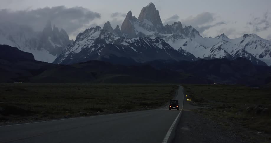 A truck drives down the road towards a snowy mountain