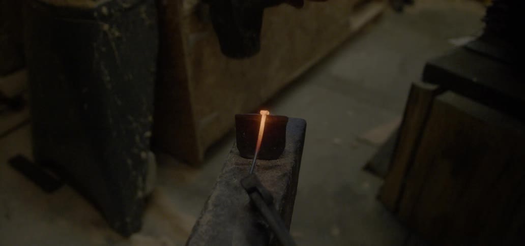 A man is using a sledge hammer to form a piece of metal on an anvil