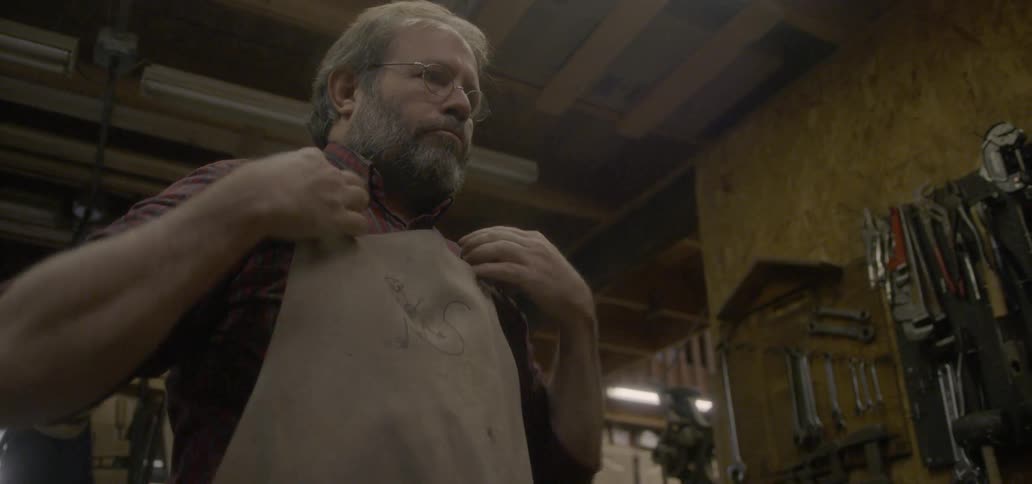 A man puts on an apron in his shop