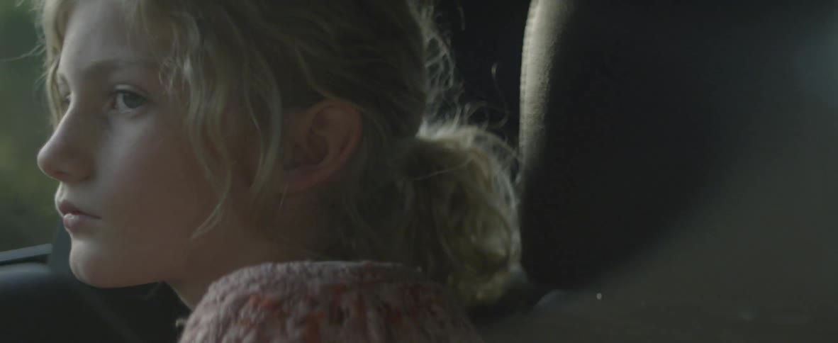 A girl is staring into space as she rides in a moving vehicle in daylight