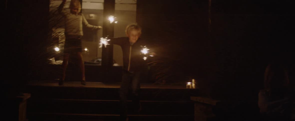 Children run around the yard at night with sparklers