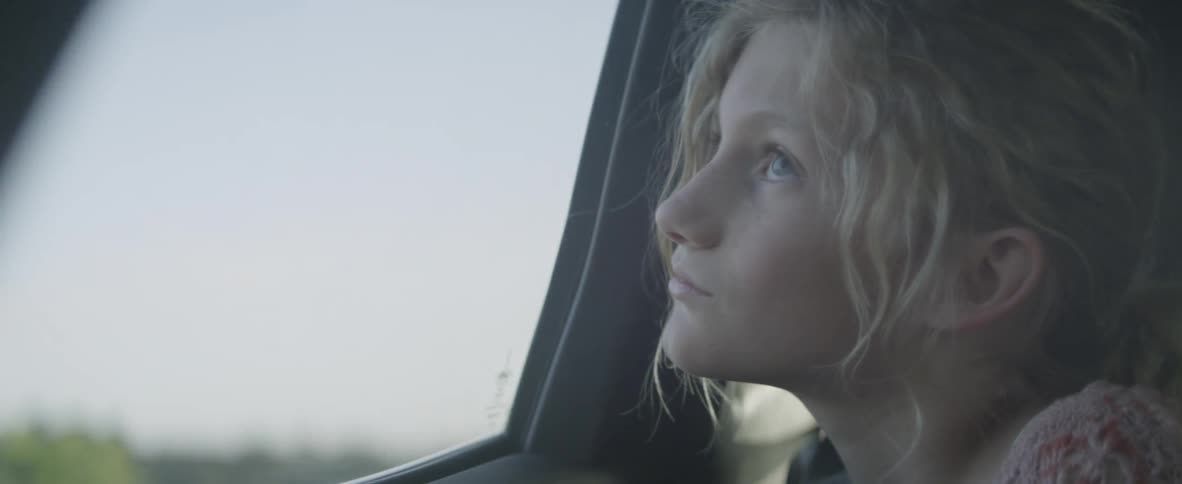 A young girl looks around from the backseat of a car