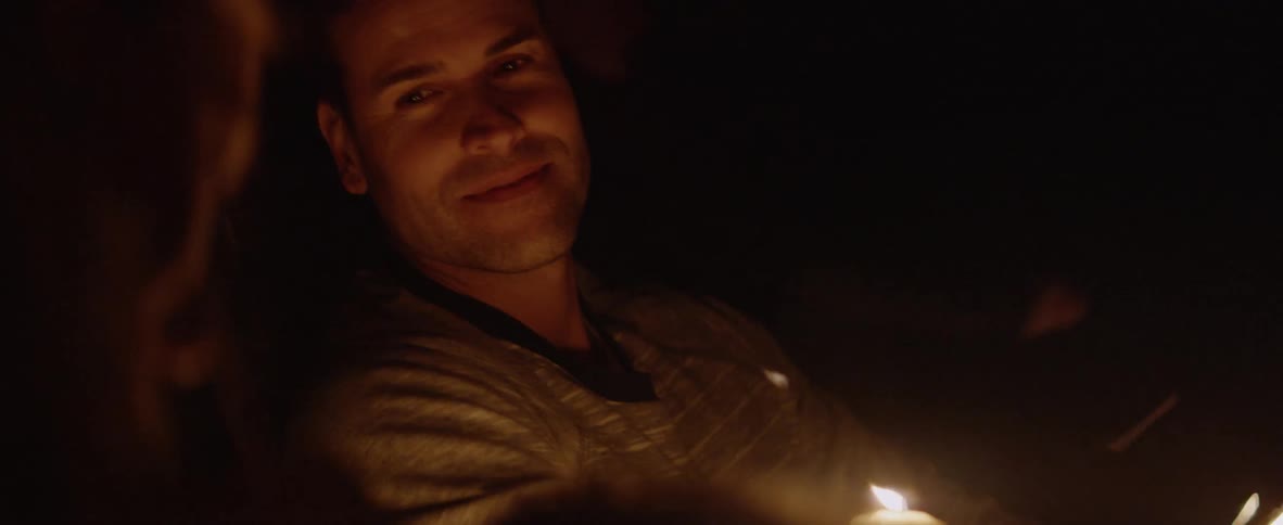 A man smiles and talks with someone at the campfire