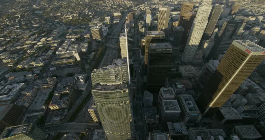 The morning sunshine reflects off of a tall city building as cars travel around