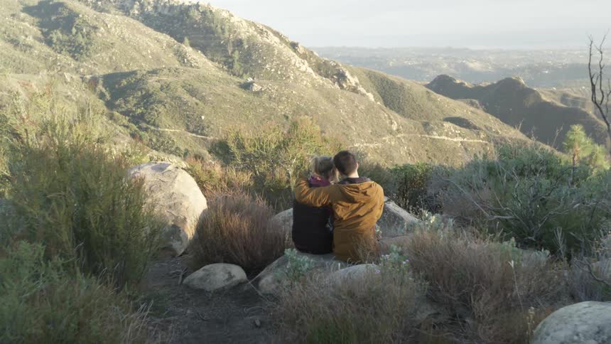 Man and woman sitting on a rock by a cliff