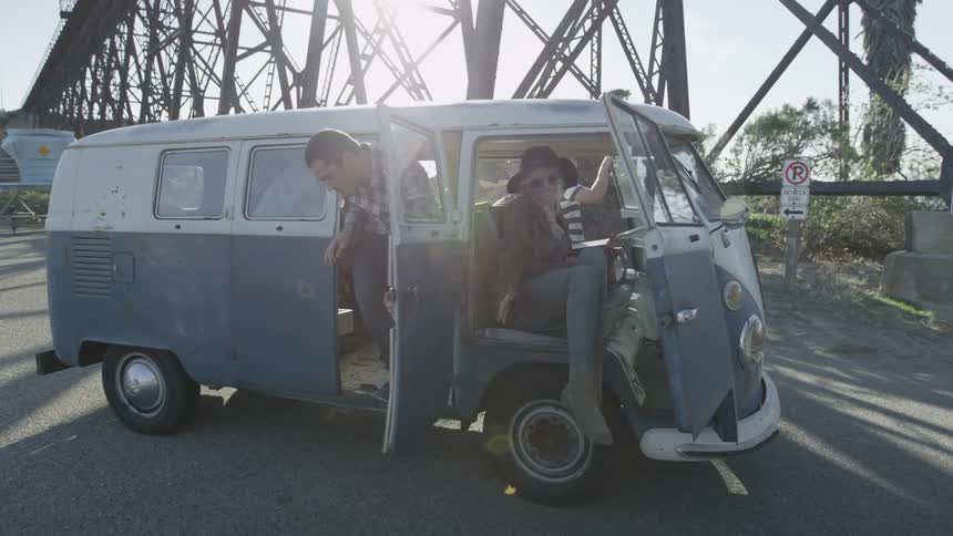 An old, vw van driving through a lot and stopping under a bridge
