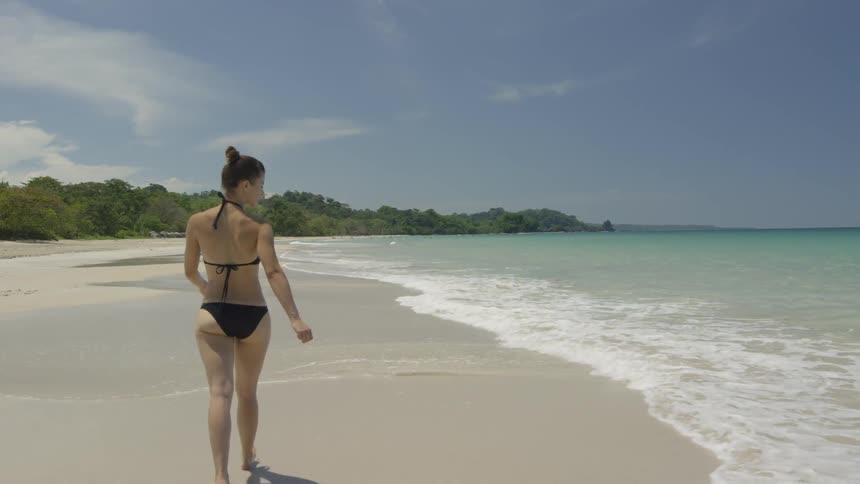 A woman walks on a beach in a bikini