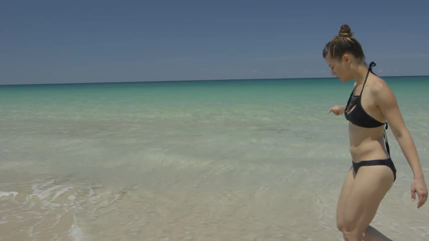 A woman walks on a beach in a bikini