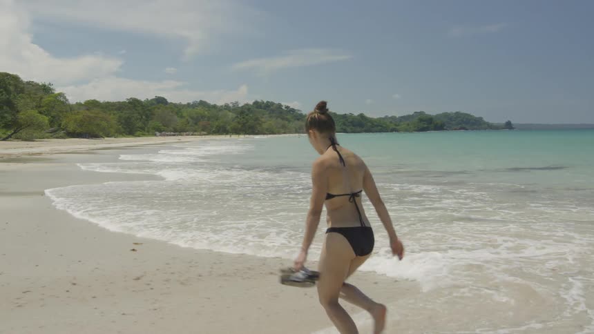 A woman carries her slippers on the beach