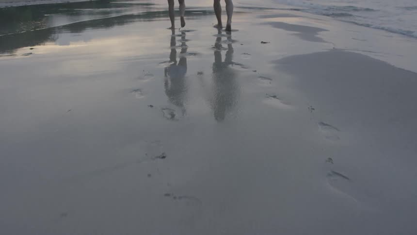 Man and woman hold hands as they walk on a beach